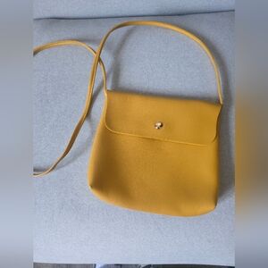 Mustard color cross body purse with tan interior lining. Single snap fastener vi